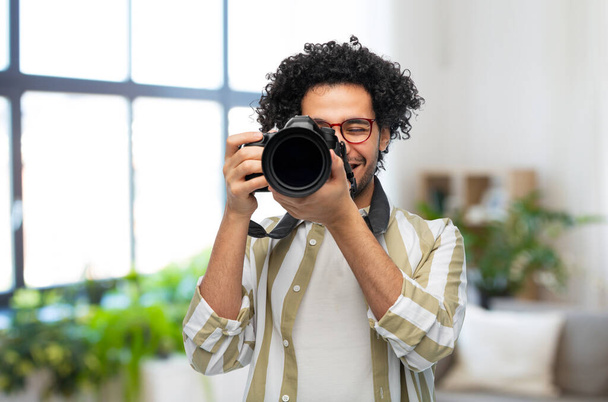 photography, profession and people and concept - happy smiling man or photographer in glasses with digital camera over home room background - Фото, изображение