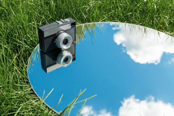 photography and nature concept - camera and blue sky reflection in round mirror on grass - Foto, immagini