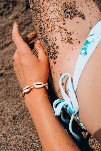 As mãos de mulher com jóias de concha na areia. Areia nas mãos na praia. Conceito de viagem e férias. Pernas finas femininas. Verão relaxar - Foto, Imagem