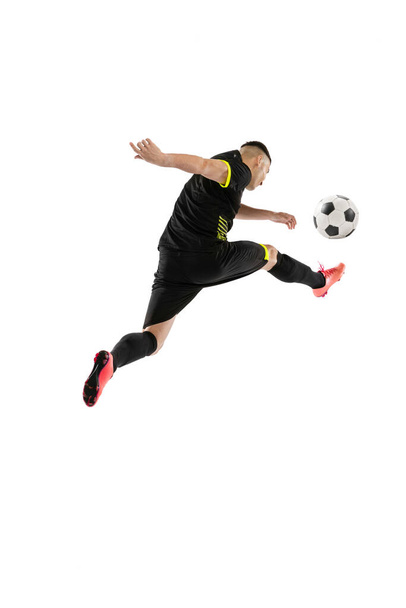 Kick. Dynamic portrait of professional male football soccer player training isolated on white background. Concept of sport, goals, competition, hobby, ad. Sportsmen wearing black football kit - Foto, imagen