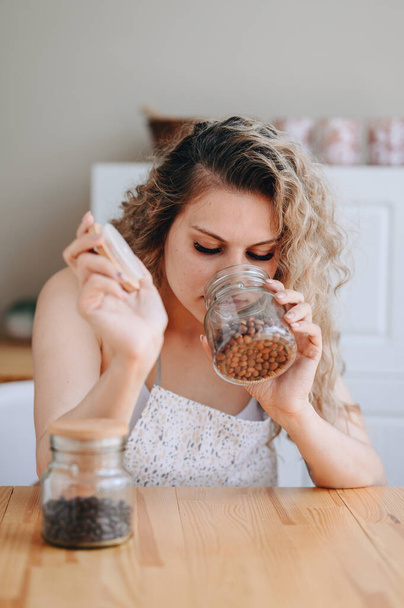 Close-up vertical portrait of a housewife sits at a table, looks and sniffs a jar of groceries, is going to cook dinner, breakfast. home lifestyle - Фото, изображение