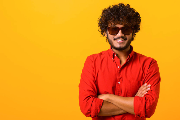 Portrait of happy satisfied handsome young man in shirt standing with crossed arms and looking at camera with toothy smile. Indoor studio shot on orange background - Foto, imagen