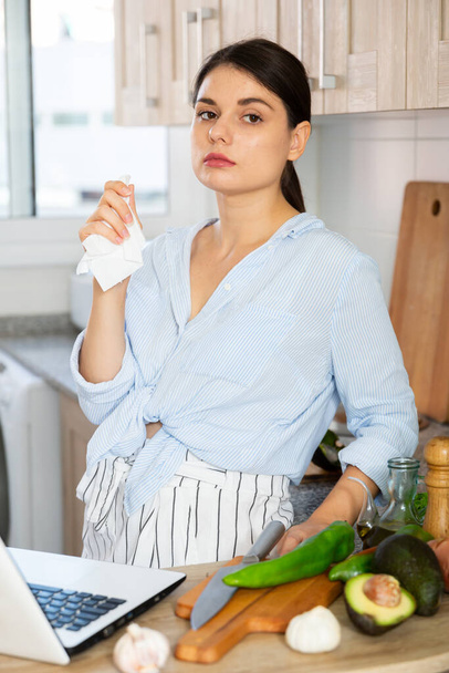 портрет расстроенной молодой женщины домохозяйки, стоящей дома на кухне перед приготовлением пищи - Фото, изображение