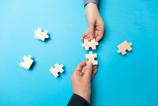 Two hands connect puzzles on a blue background. Cooperation and teamwork in business. Collaboration people for success. - Foto, imagen