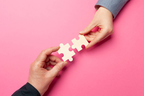 Two hands connect puzzles on a pink background. Cooperation and teamwork in business. Collaboration people for success. - Zdjęcie, obraz