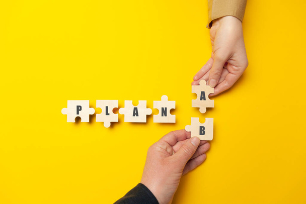 Hands of businessmen folded the word "Plan A B" from puzzles on a yellow background. Success strategy and alternative problem solving. - Φωτογραφία, εικόνα