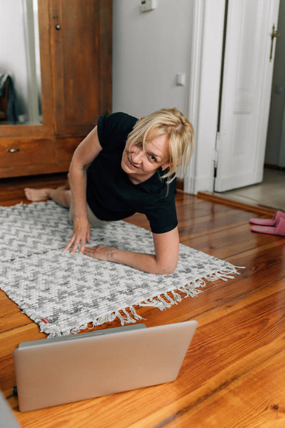 volwassen vrouw thuis doen sport yoga op de vloer met laptop online klassen. Hoge kwaliteit foto - Foto, afbeelding
