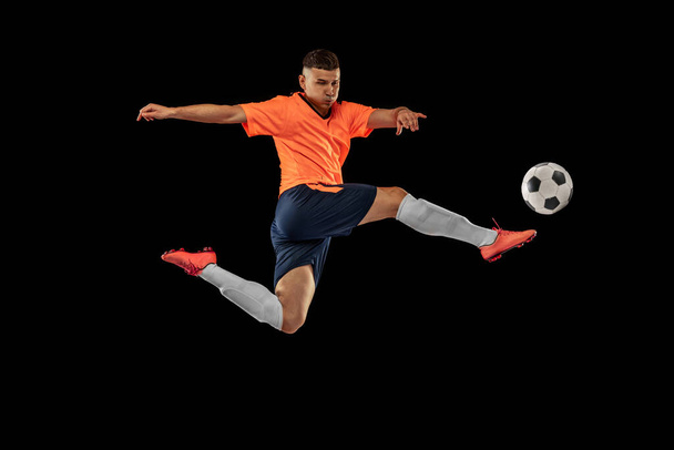 Dynamic portrait of professional male football soccer player in motion isolated on dark background. Concept of sport, goals, competition, hobby, ad. Sportsmen wearing orange-blue football kit - Фото, изображение