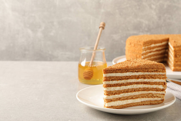 Slice of delicious layered honey cake served on grey table. Space for text - Zdjęcie, obraz
