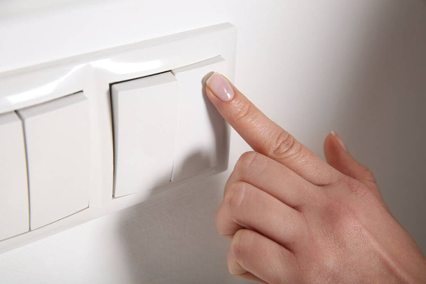 Woman turning off light switch indoors, closeup. Energy saving concept - Foto, immagini
