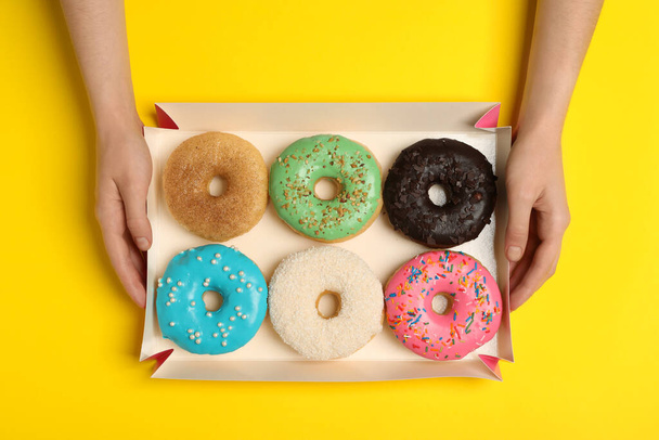 Woman with box of delicious donuts on yellow background, top view - Photo, Image