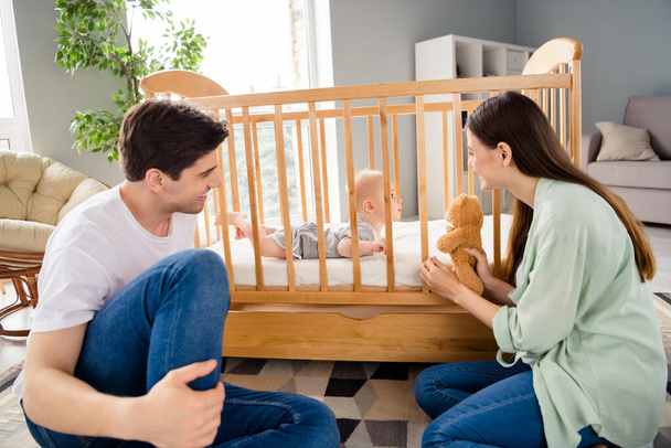 Portrait of peaceful idyllic family parents hold soft bear toy playing toddler bed free time indoors. - Фото, изображение