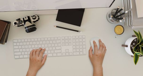 Overhead shot, A female hands typing on computer keyboard on a modern office workspace with camera, stationery, office supplies and decor on white table background. 3d rendering, 3d illustration - 写真・画像