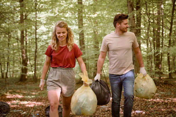 Καυκάσια ενήλικη γυναίκα και άντρας που κρατούν σακούλες σκουπιδιών στο δάσος  - Φωτογραφία, εικόνα