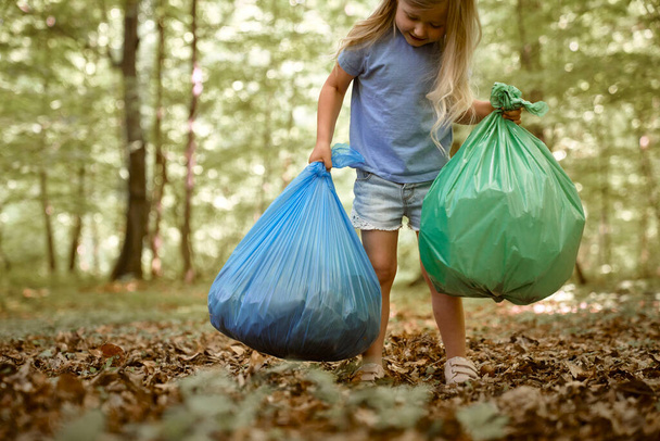 Кавказька дівчинка несе мішки з сміття в лісі.  - Фото, зображення