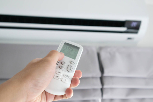 Hand met afstandsbediening gericht op airconditioner - Foto, afbeelding