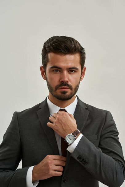Partial of confident caucasian entrepreneur straighten tie of his suit and looking at camera. Concept of modern successful male lifestyle. Isolated on white background. Studio shoot. Copy space - Valokuva, kuva