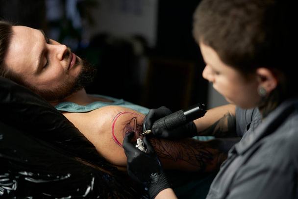 Tatuaje artista dibujo en brazo del cliente  - Foto, imagen