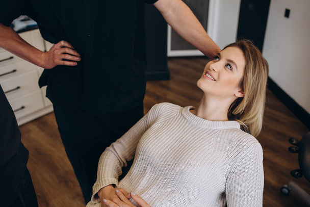 Beautiful and happy blonde woman at beauty medical clinic. She is sitting and talking with female doctor about face esthetics treatment. - 写真・画像