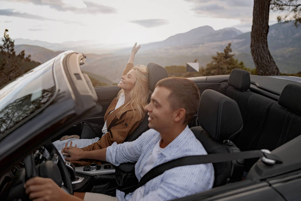 Happy couple in love roofless convertible car holding hands driving by the mountain road, side view - Foto, Imagen