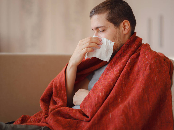 Coronavirus. Sick man of corona virus lying down in sofa and recovery from illness in home. Blowing his nose. The concept of high temperatures. The person is seriously ill. - Fotografie, Obrázek