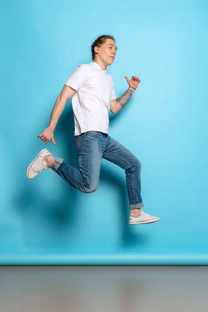 Happiness. Full-length portrait of young man, student in casual style outfit jumping isolated on blue background. Human emotions, facial expression concept. Trendy colors. Looks happy, delighted - Fotografie, Obrázek