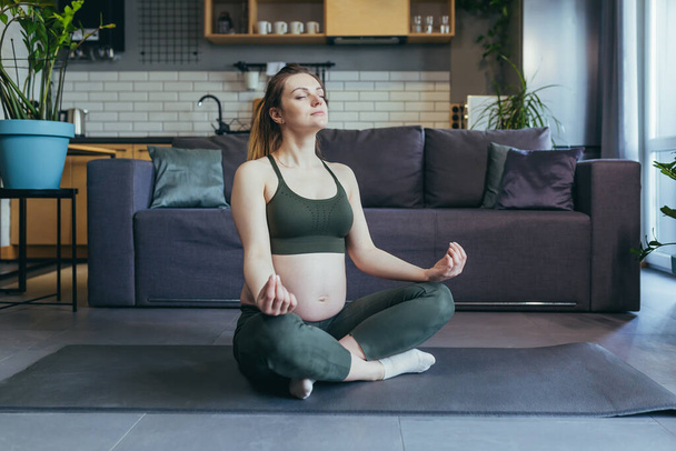 A pregnant woman meditates and practices yoga in a lotus position at home - Фото, зображення