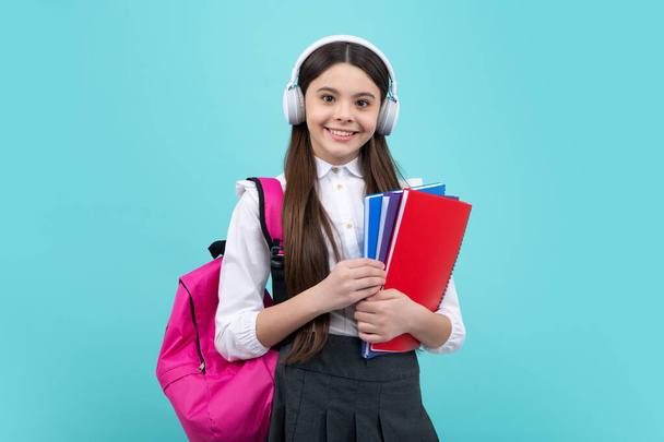 Schoolgirl, teenage student lifestyle girl in headphones hold books on blue isolated studio background. School and music education concept - Fotoğraf, Görsel