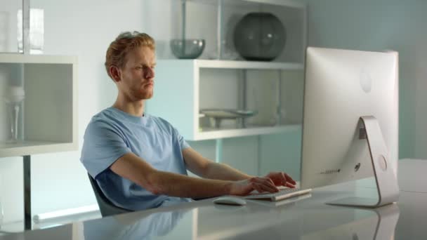 IT dolgozó gépel asztali számítógép otthoni irodai közelkép. Távoli kilátás a munkahelyre. Koncentrált üzletember jóképű vörös hajú férfi szörfözik otthon. Komoly szabadúszó diák elemzése adatkereső képernyő. - Felvétel, videó