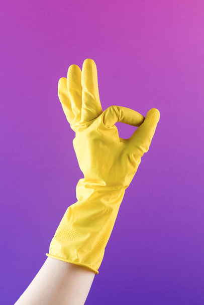 Käsi keltainen kumihanska näyttää OK ele violetti tausta lähikuva. Siivouspalvelu. Helppo kotityöt ja rutiini askareita - Valokuva, kuva
