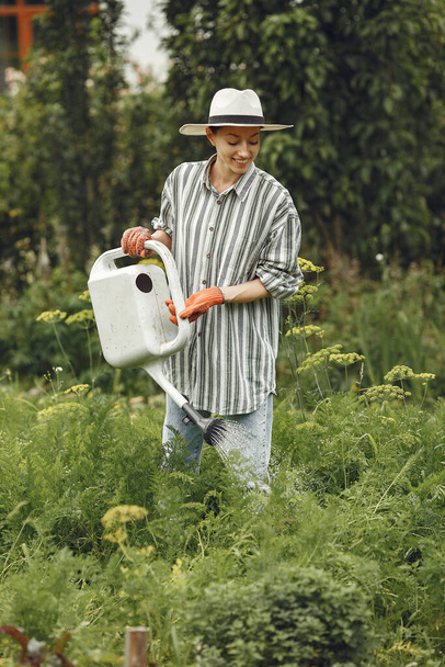 Gardening in summer. Woman watering flowers with a watering can. Girl wearing a hat. - Foto, Bild