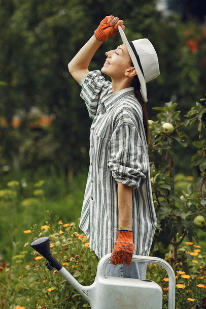 Gardening in summer. Woman watering flowers with a watering can. Girl wearing a hat. - Fotó, kép