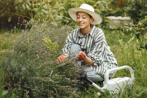 Gardening in summer. Woman watering flowers with a watering can. Girl wearing a hat. - Foto, Imagen