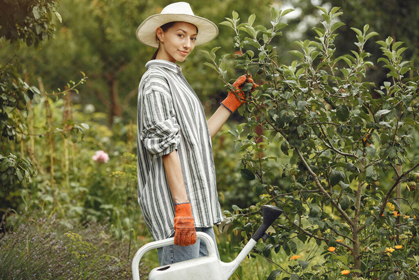 Gardening in summer. Woman watering flowers with a watering can. Girl wearing a hat. - Zdjęcie, obraz