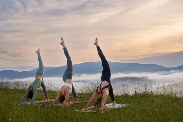 Group of three young women in sport clothes having yoga practice with amazing view on mountains. Concept of people, training and healthy lifestyles.  - Foto, Imagem