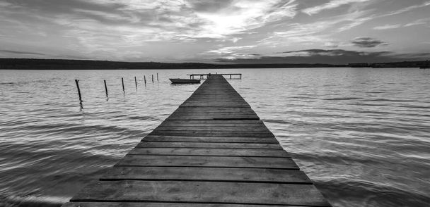 Spannende schemering aan de kust met houten pier en afgemeerde boot - Foto, afbeelding