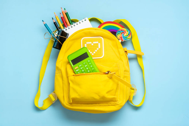 Vissza az iskolába, oktatási koncepció Sárga hátizsák iskolai felszereléssel - notebook, tollak, radír szivárvány, kék háttérrel elszigetelt számok Felülnézet Másolás. - Fotó, kép