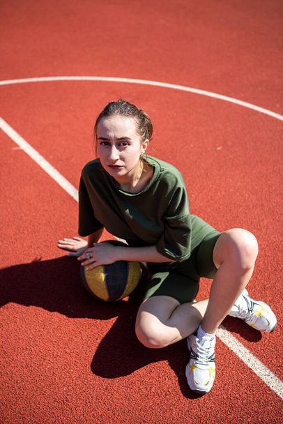 Aantrekkelijke jonge slanke vrouw die poseert op een basketbalveld met een basketbal. stedelijke levensstijl. Hete zomerdag. sport voor de gezondheid - Foto, afbeelding