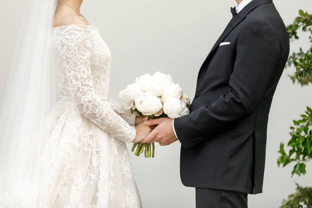 Νύφη και γαμπρός κρατιούνται χέρι χέρι. Νύφη με γαμήλιο μπουκέτο - Φωτογραφία, εικόνα