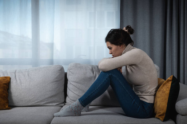 Young sad woman with broken heart sitting alone at home suffering from depression anxiety and bad mental condition. Female having hard time and burnout of overthinking and worry for her job situation - Valokuva, kuva