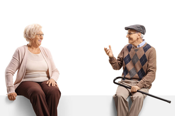 Elderly man and woman sitting on a blank panel and having a conversation isolated on white background - Φωτογραφία, εικόνα