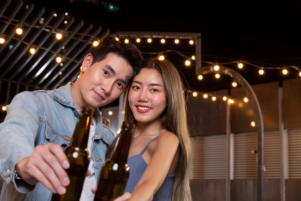 happy asian teenager couple man and woman in love drinking beer alcohol and toasting bottle in celebration party. young happy couple love and romantic at first date. - Photo, Image
