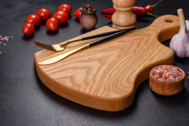 Пустая тарелка с ножом, вилкой или ложкой с деревянной доской для резки на темном бетонном фоне. Подготовка приборов и ингредиентов для домашней кухни - Фото, изображение
