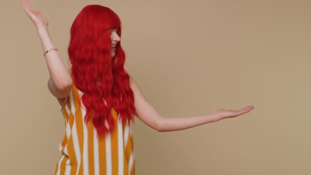 Güzel kızıl saçlı kadın boş bir yeri işaret ediyor ticari metinler için reklam alanı, ürün tanıtımı için fotokopi alanı. Genç kızıl kız. Bej arka planda kapalı stüdyo çekimleri - Video, Çekim