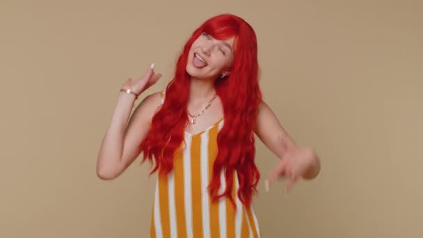 Funny joyful sincere redhead woman 20s in tank top making playful silly facial expressions and grimacing, fooling around showing tongue. Young beautiful ginger girl isolated alone on beige background - Footage, Video
