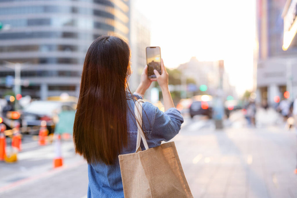Femme utiliser un téléphone mobile pour prendre des photos sous la vue du coucher du soleil en ville - Photo, image