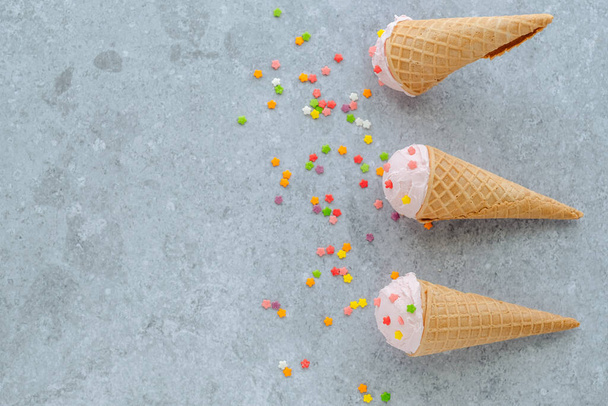 Pink ice cream in the horn sprinkle with colored stars on a gray background. Summer and sweet menu concept, flat lay, space for text . High quality photo - Photo, image