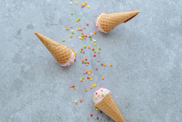 Pink ice cream ball in the horn sprinkle with colored stars on a gray background. Summer and sweet menu concept, flat lay. High quality photo - Foto, Imagem