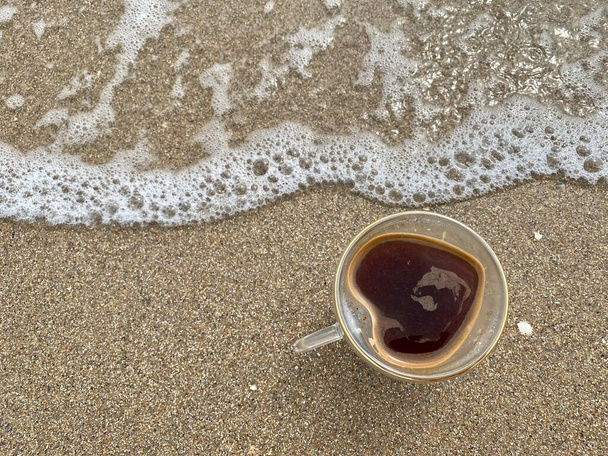 Una tazza insolita di caffè a forma di cuore in piedi sulla sabbia vicino al mare, perfetto concetto di amore estivo, concetto di vacanza o agenzia turistica. - Foto, immagini