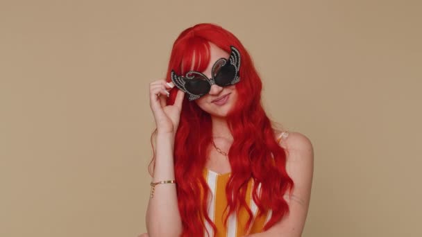 Portrait of seductive cheerful redhead woman in tank top wearing fashion sunglasses, charming smile. People happy emotions. Young lovely ginger girl posing isolated alone on beige studio background - Footage, Video